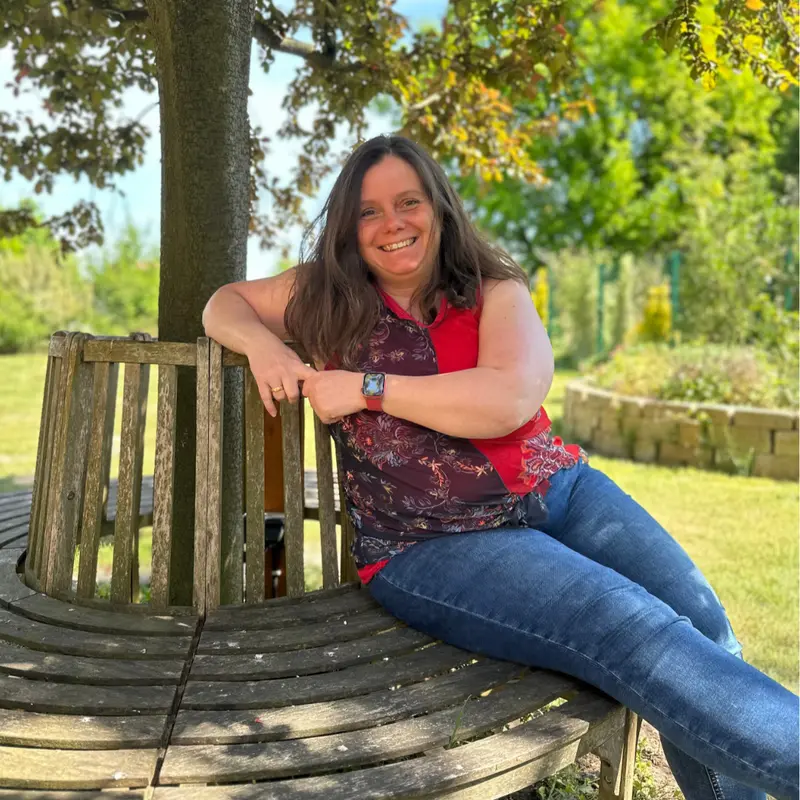 Melanie Klußmann-Bülter sitzt lächelnd auf einer Holzbank im Garten